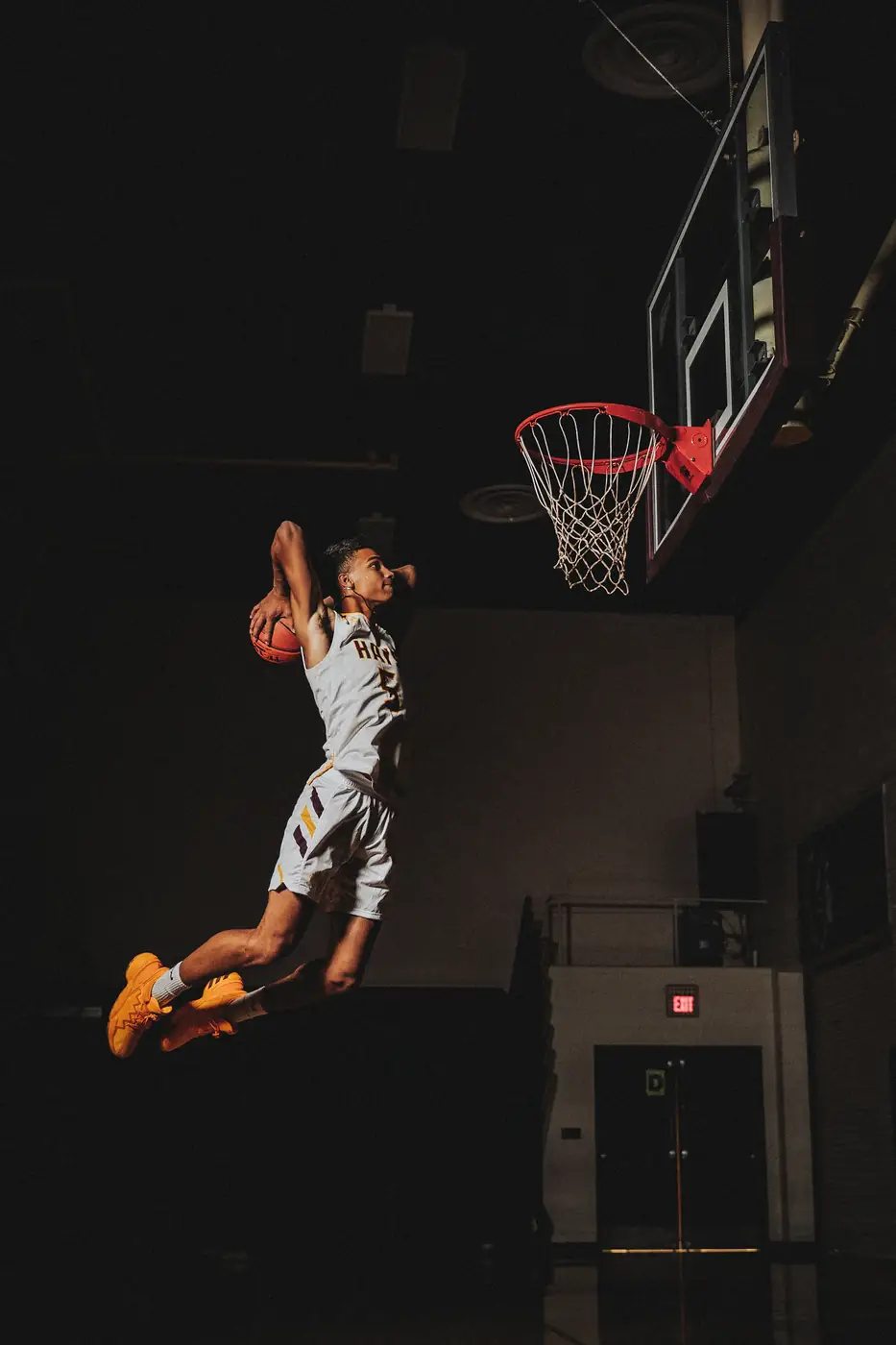 Ein Basketballspieler springt in einer dunklen Halle zum Korb.
