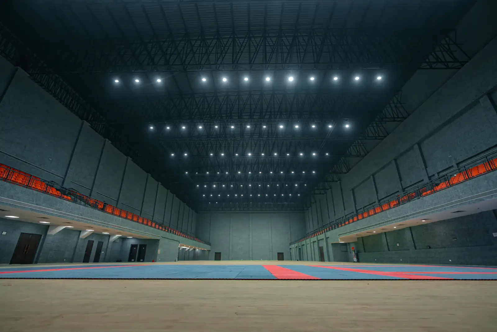Große, leere Sporthalle mit Tribünen unter Deckenlicht.